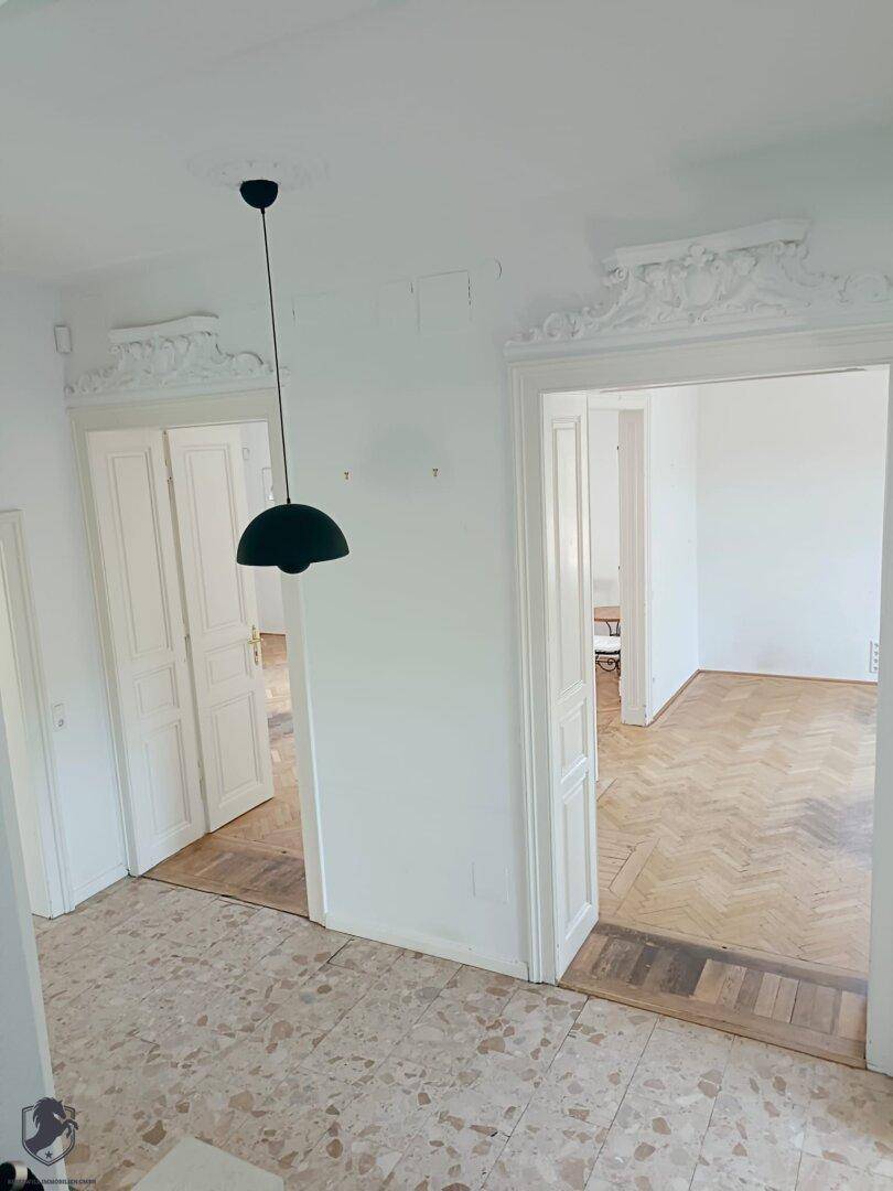 Heller Flur mit Terrazzoboden und hohen Türen, die zu weiteren Räumen führen.