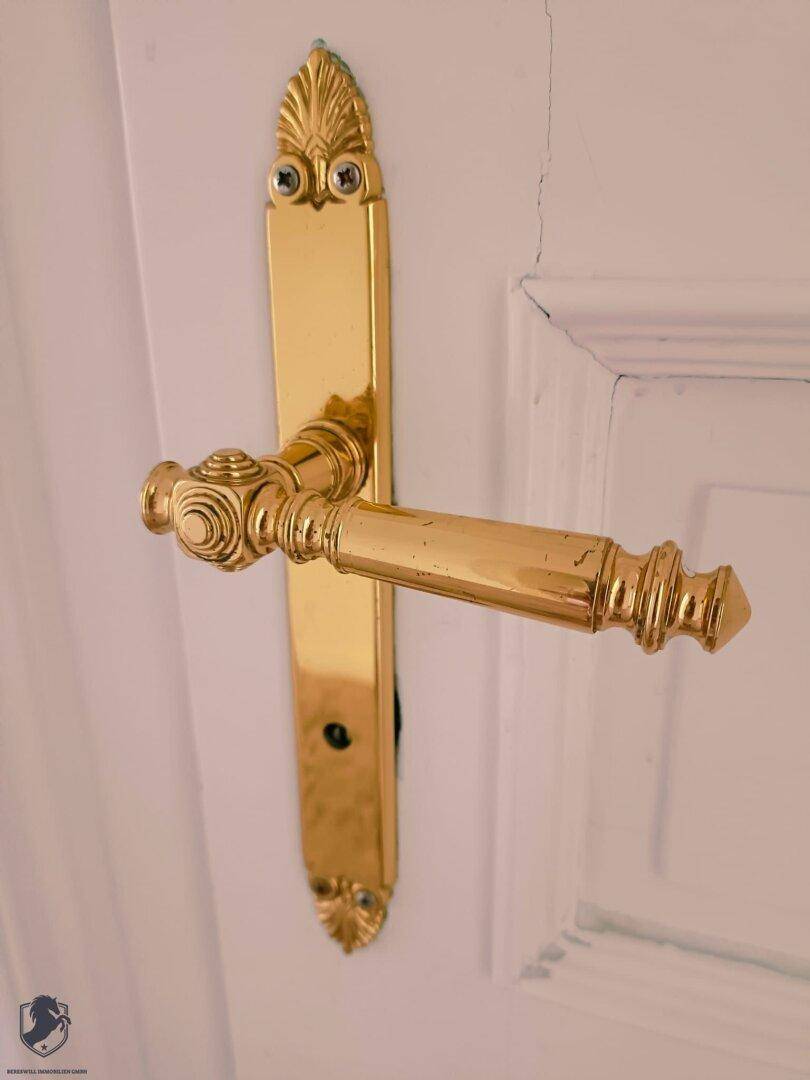 Detailaufnahme einer eleganten, goldenen Türfalle an einer weißen Holztür.