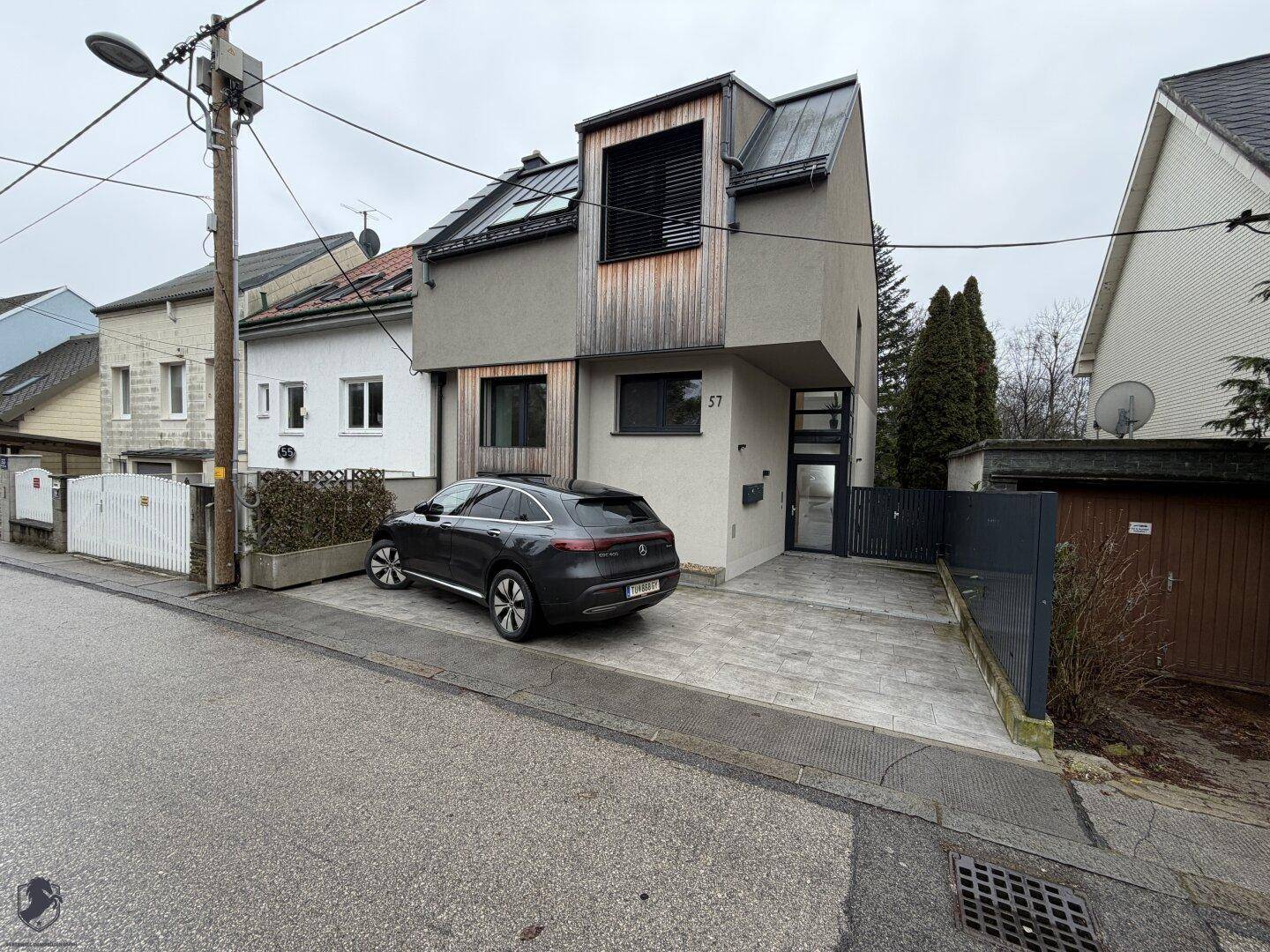 Moderne Stadtvilla mit Holzverkleidung und gepflasterter Einfahrt, umgeben von Bäumen.