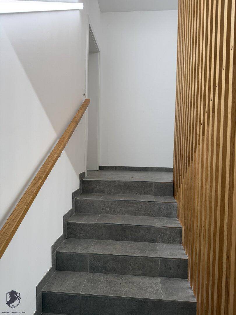 Moderner Treppenaufgang mit Holzlamellenwand und Fliesenboden, der in die obere Etage führt.