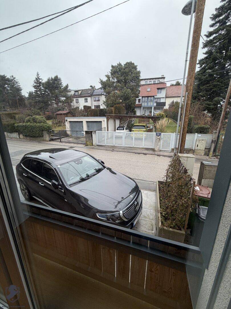 Blick aus dem Fenster auf die Straße mit geparktem Auto und umliegenden Häusern.