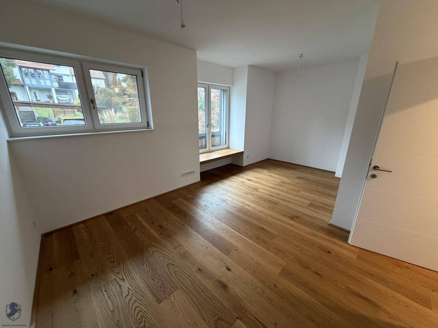 Geräumiges Zimmer mit großen Fenstern und Holzboden, bietet viel natürliches Licht.