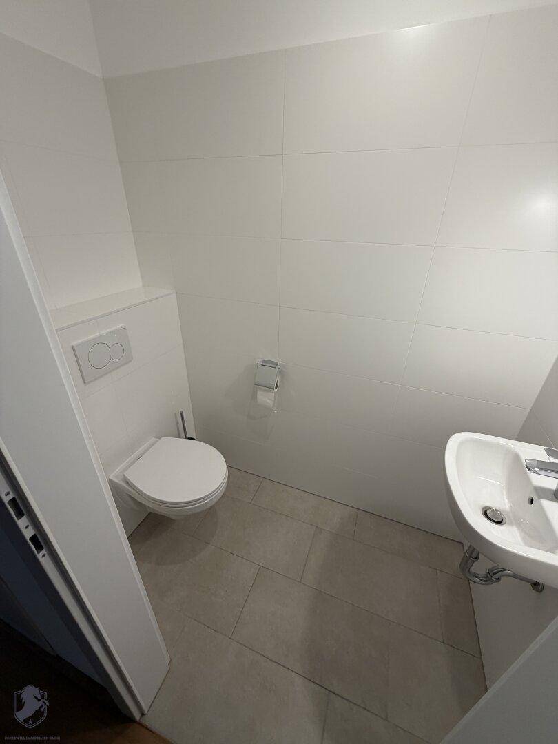 Kleines Gäste-WC mit modernem Wand-WC und Handwaschbecken, hell gefliest.