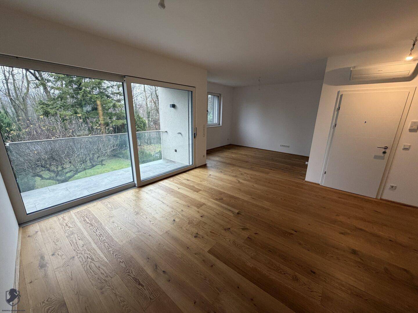 Heller Wohnbereich mit Holzboden und großem Schiebefenster zum Balkon, bietet viel Licht.