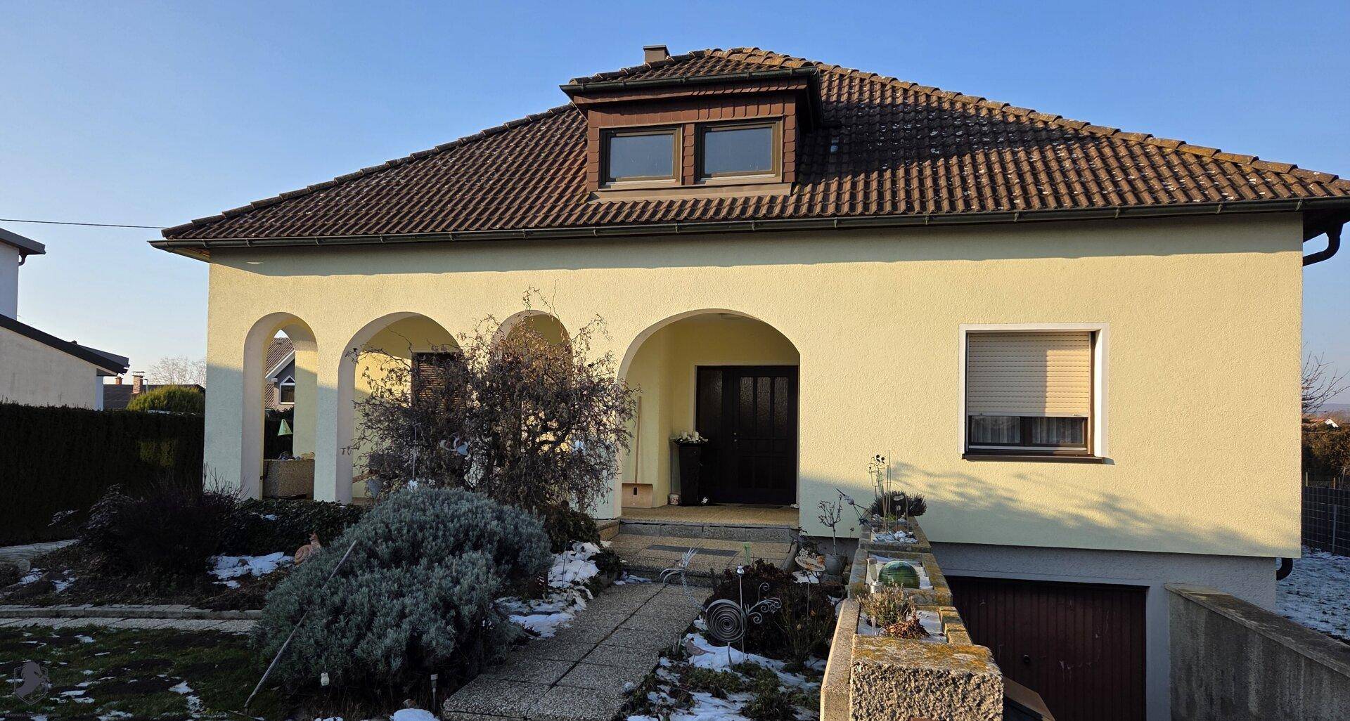 Vorderansicht des Hauses mit Eingangsbereich, Bogenfenstern und Vorgarten im Winter.