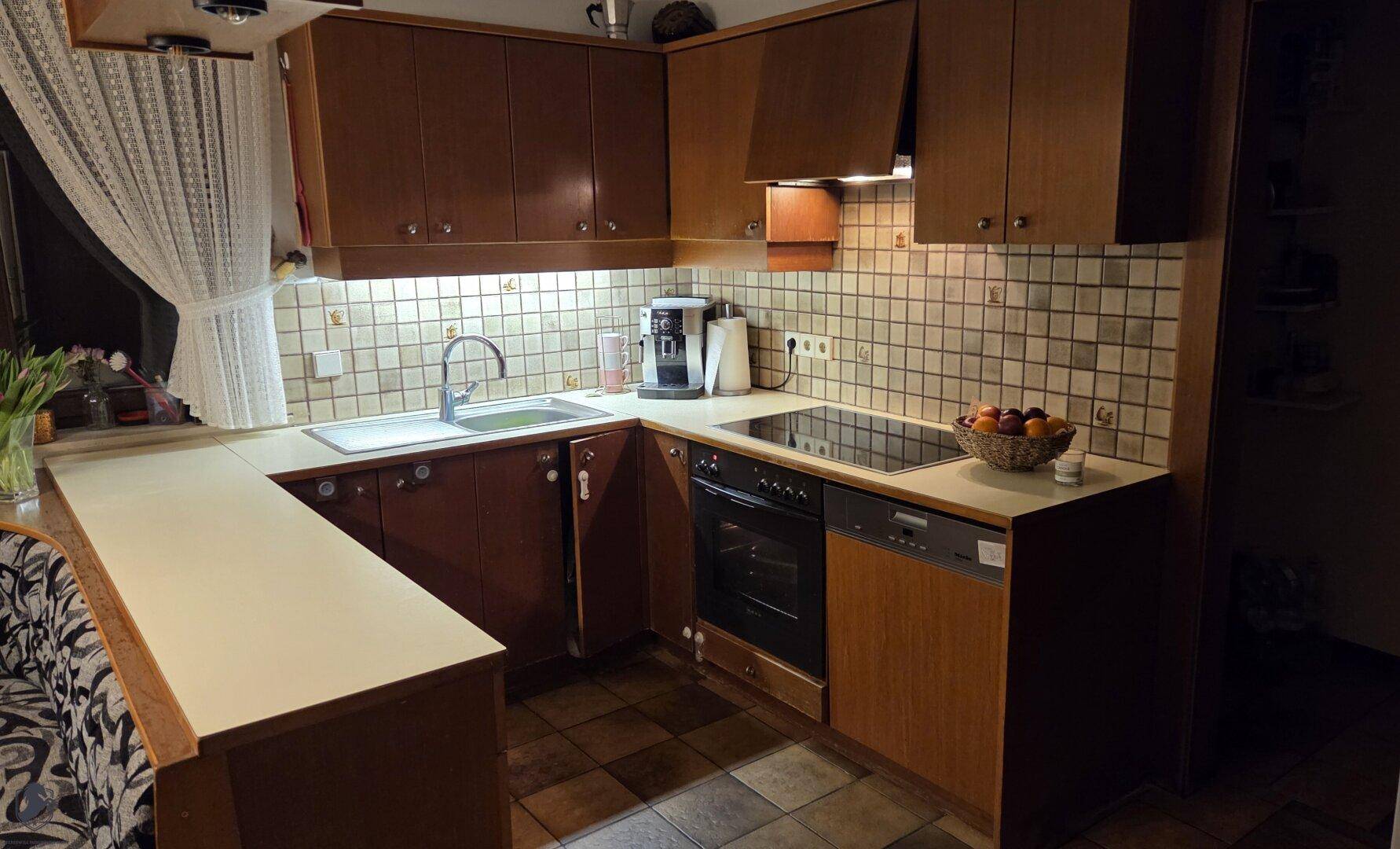 Funktionale Küche mit dunklen Holzfronten, heller Arbeitsplatte und integrierten Geräten und Fliesenboden.