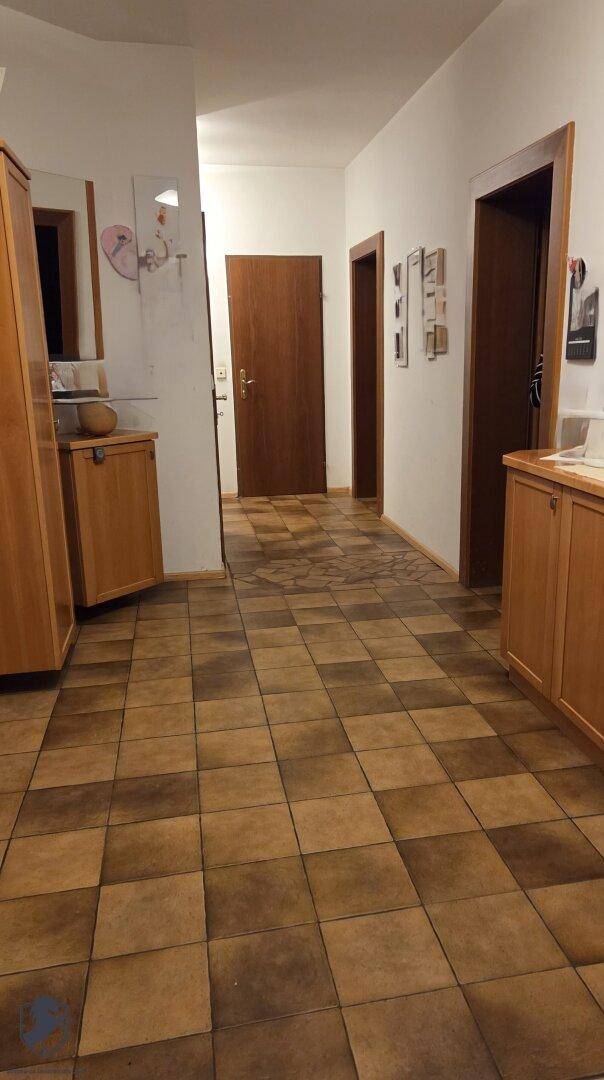 Heller Flur mit braunen Fliesen und Holzmöbeln, der zu weiteren Räumen im Haus führt.