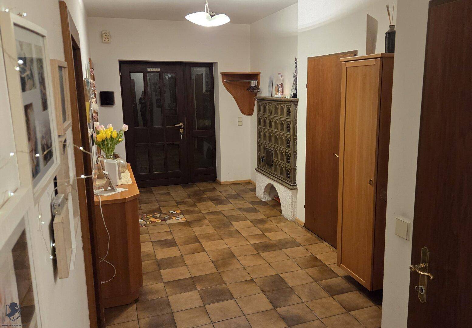 Geräumiger Flur mit Fliesenboden, traditionellem Kachelofen und dunkler Eingangstür.