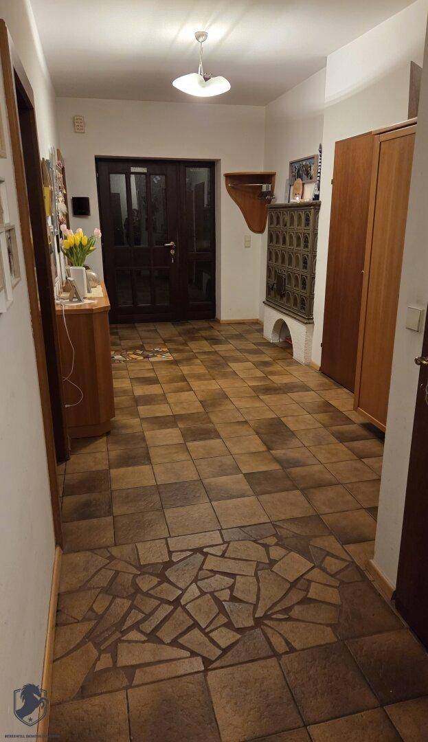 Eingangsbereich mit gemustertem Fliesenboden, Kachelofen und dunkler Eingangstür.