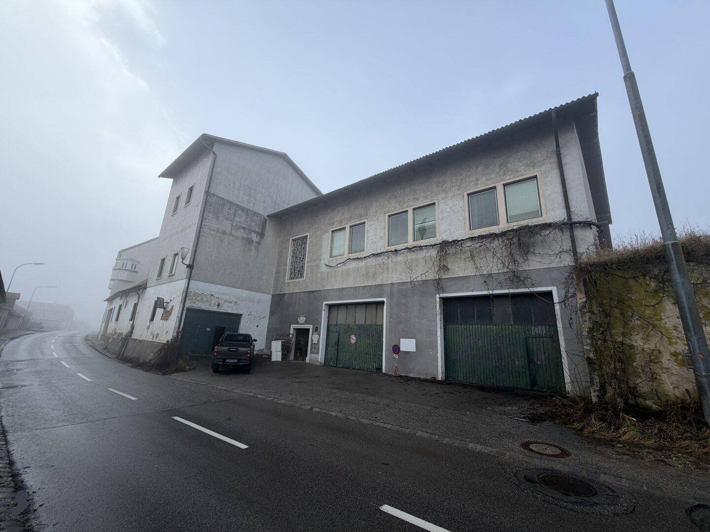 Gesamtansicht des alten Industriegebäudes mit Garagentoren und Fenstern unter einem bewölkten Himmel.