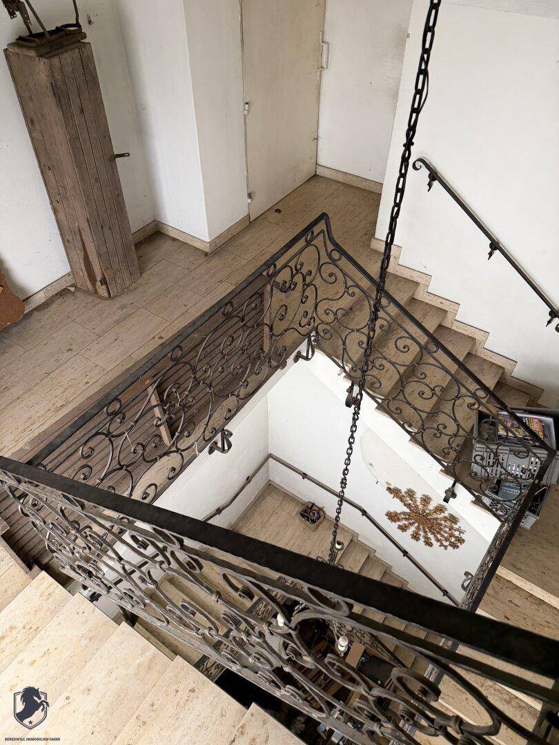 Treppenhaus mit elegantem schmiedeeisernem Geländer und hellen Steinstufen, das sich über mehrere Etagen erstreckt.