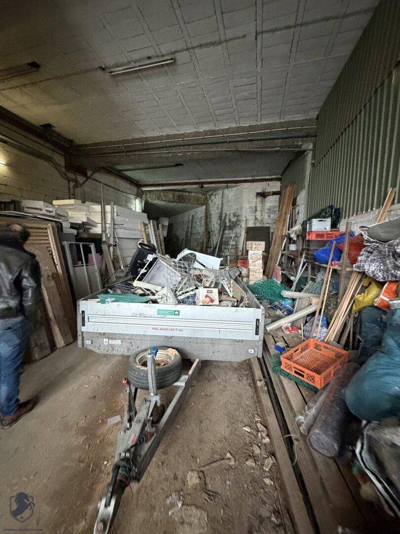 Überfüllte Garage oder Werkstatt mit einem Anhänger, Werkzeugen und einer niedrigen Betondecke.