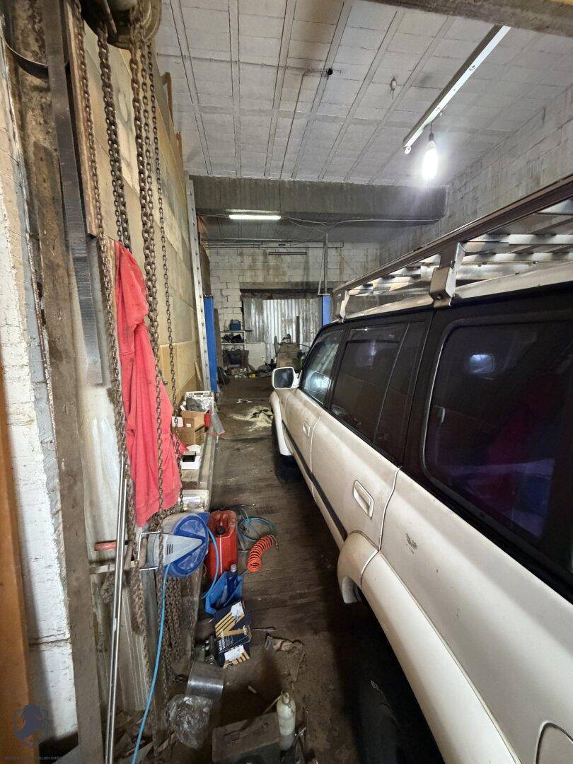 Schmaler Garagen- oder Werkstattbereich mit einem weißen SUV und Werkzeugen an der Seite.