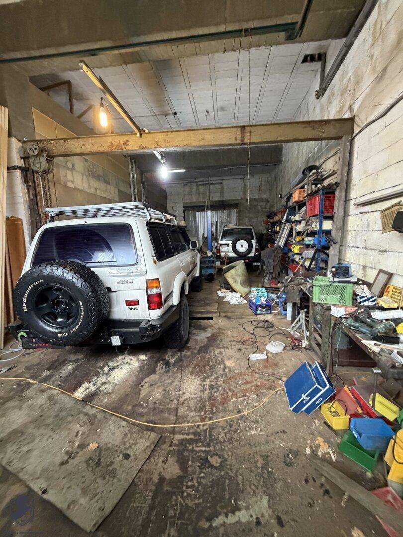Geräumige Garage oder Werkstatt mit einem weißen SUV, Regalen voller Werkzeuge und sichtbaren Deckenbalken.