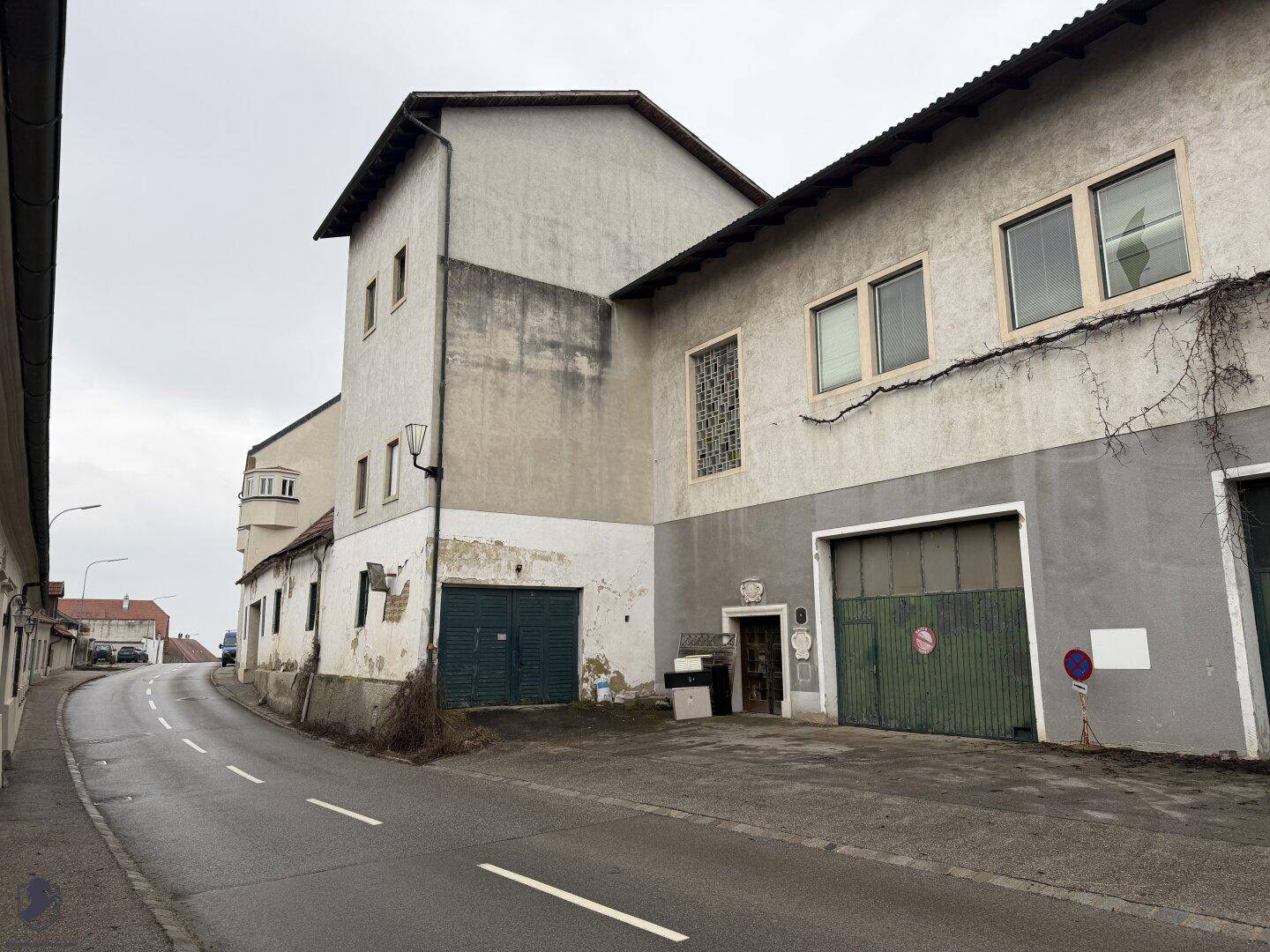 Ansicht des alten Gebäudes von der Straße mit verwitterter Fassade und mehreren Einfahrten.