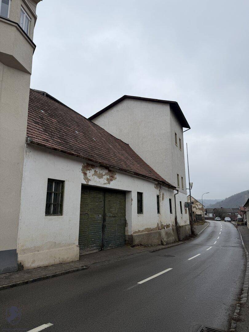 Älterer Gebäudeteil mit Ziegeldach und verputzter Fassade, daneben eine weitere Garageneinfahrt.