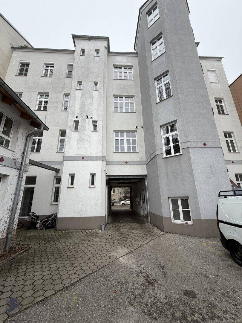 Eingangsbereich zum Innenhof eines Gebäudes mit grauer und weißer Fassade und Durchgang.