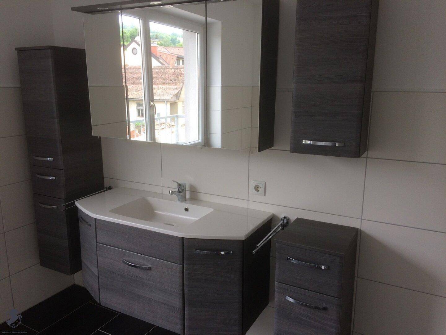 Modernes Badezimmer mit dunklen Holzmöbeln, weißem Waschbecken und Spiegelschrank.