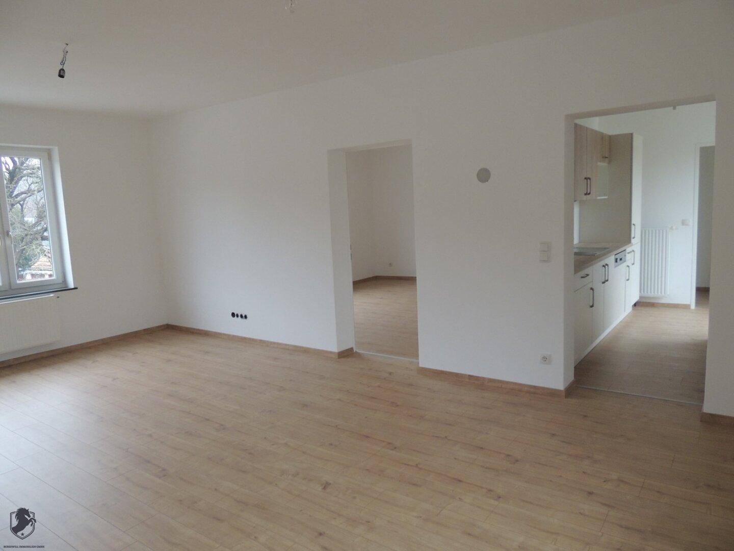 Helles Wohnzimmer mit Laminatboden und weiß gestrichenen Wänden, bereit zur Einrichtung.