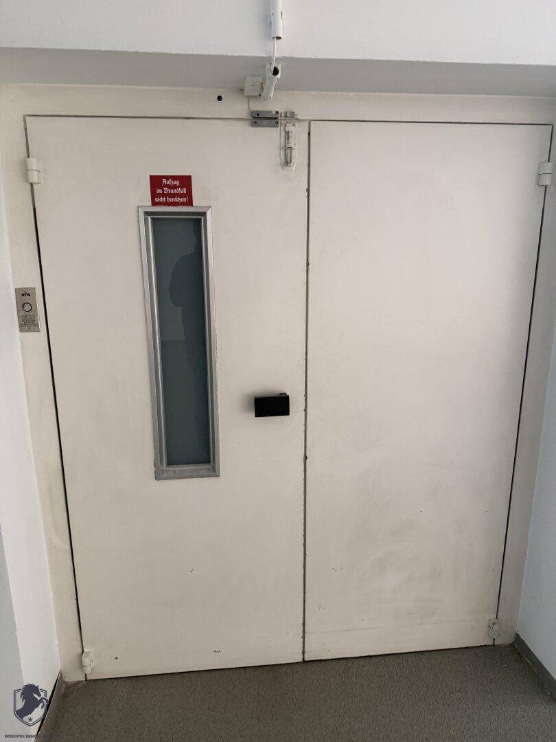Robuste Doppeltür mit kleinem Fenster und Sicherheitshinweis in einem Flur.