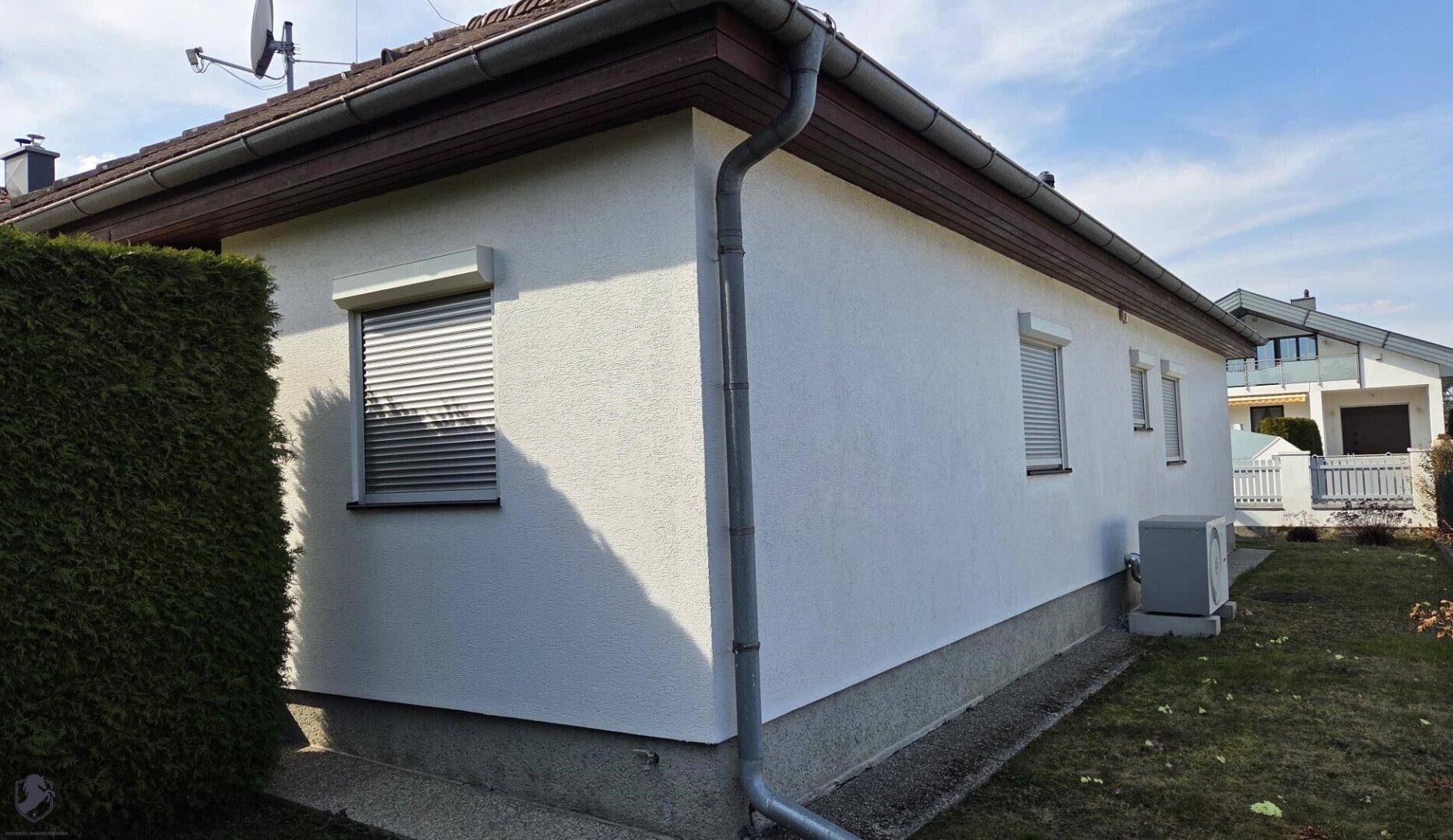 Weiße Hausfassade mit Rollläden an den Fenstern und Dachüberstand.