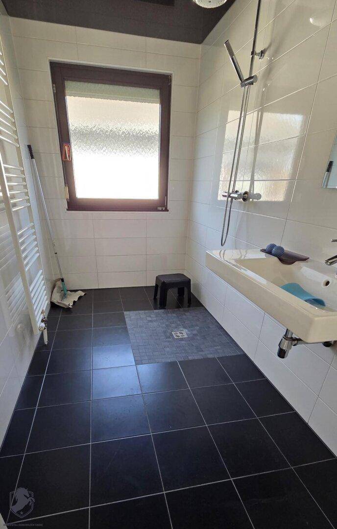 Badezimmer mit weiß gefliesten Wänden, schwarzem Boden und Duschbereich.