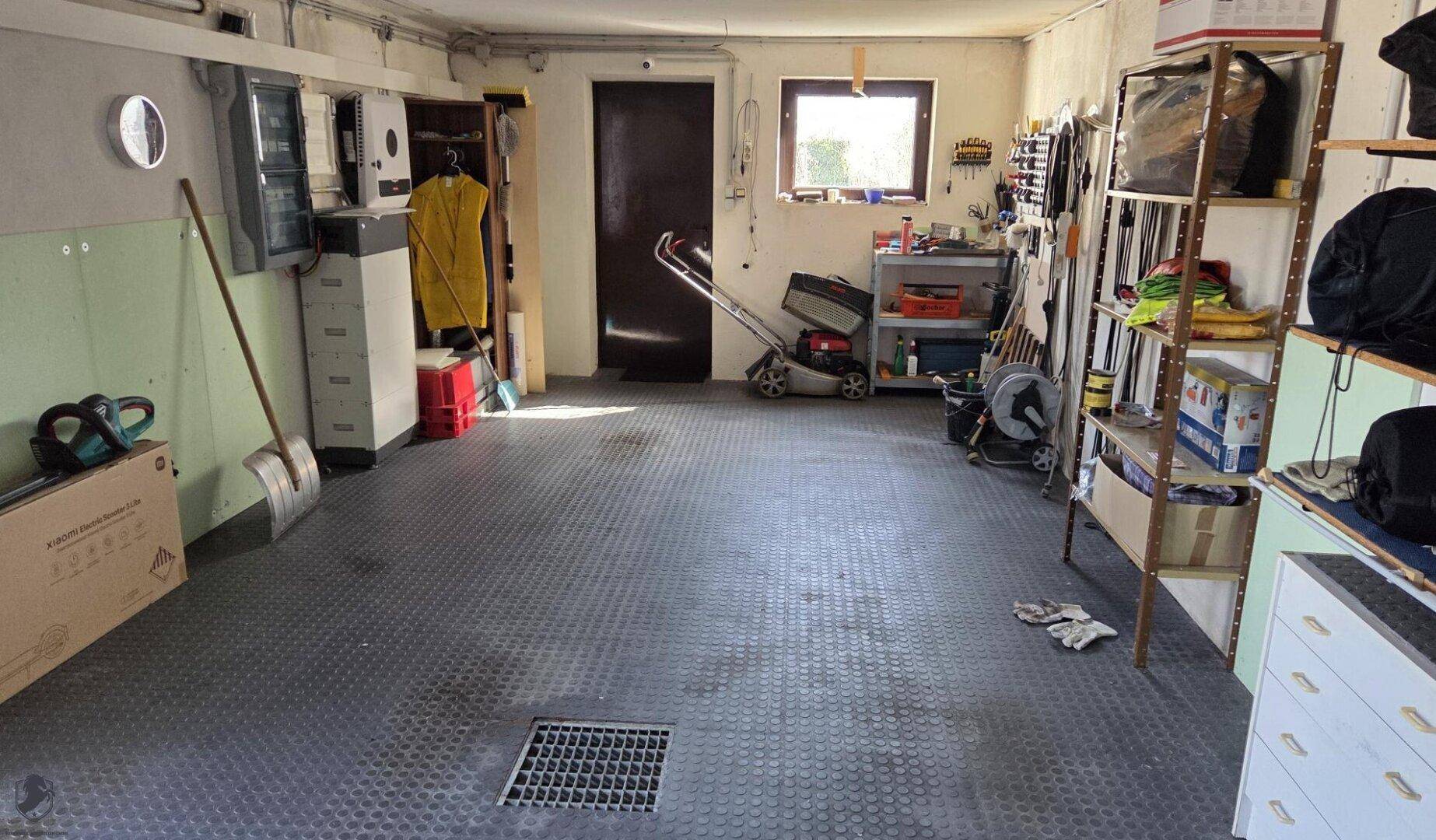 Geräumige Garage mit Werkzeugen, Regalen und einem Rasenmäher.