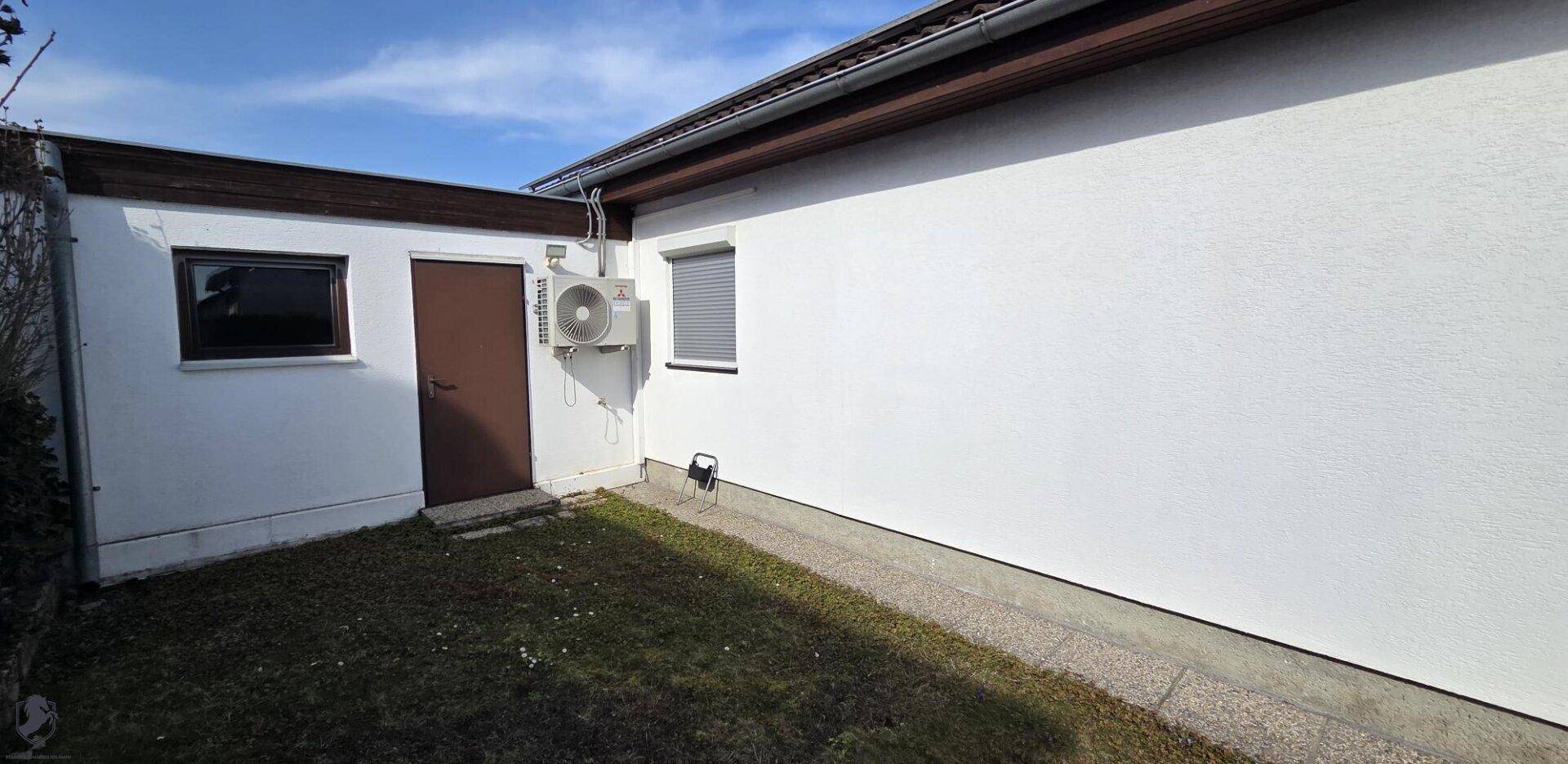 Seitenansicht des Hauses mit weißer Fassade, Tür und Klimaanlage.