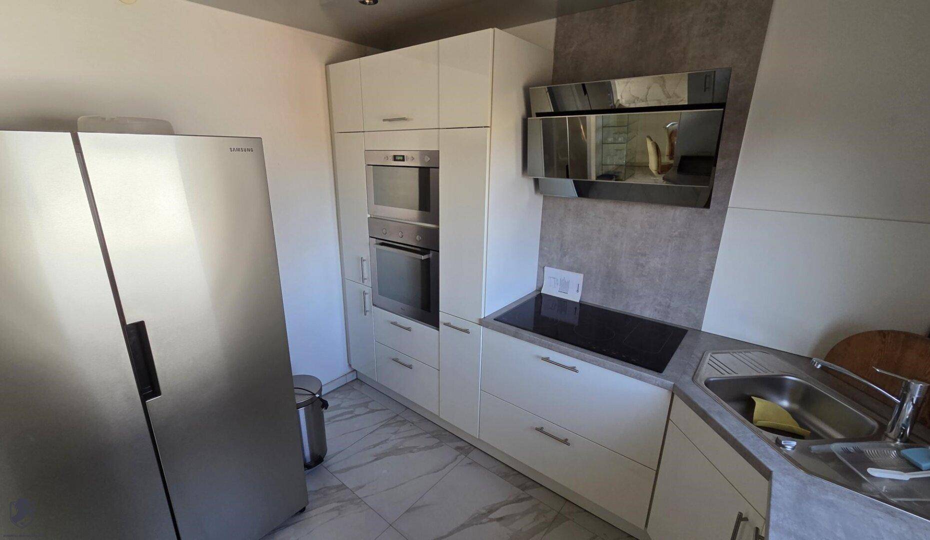Moderne Küche mit weißen Hochglanzschränken, integrierten Geräten und Induktionskochfeld.
