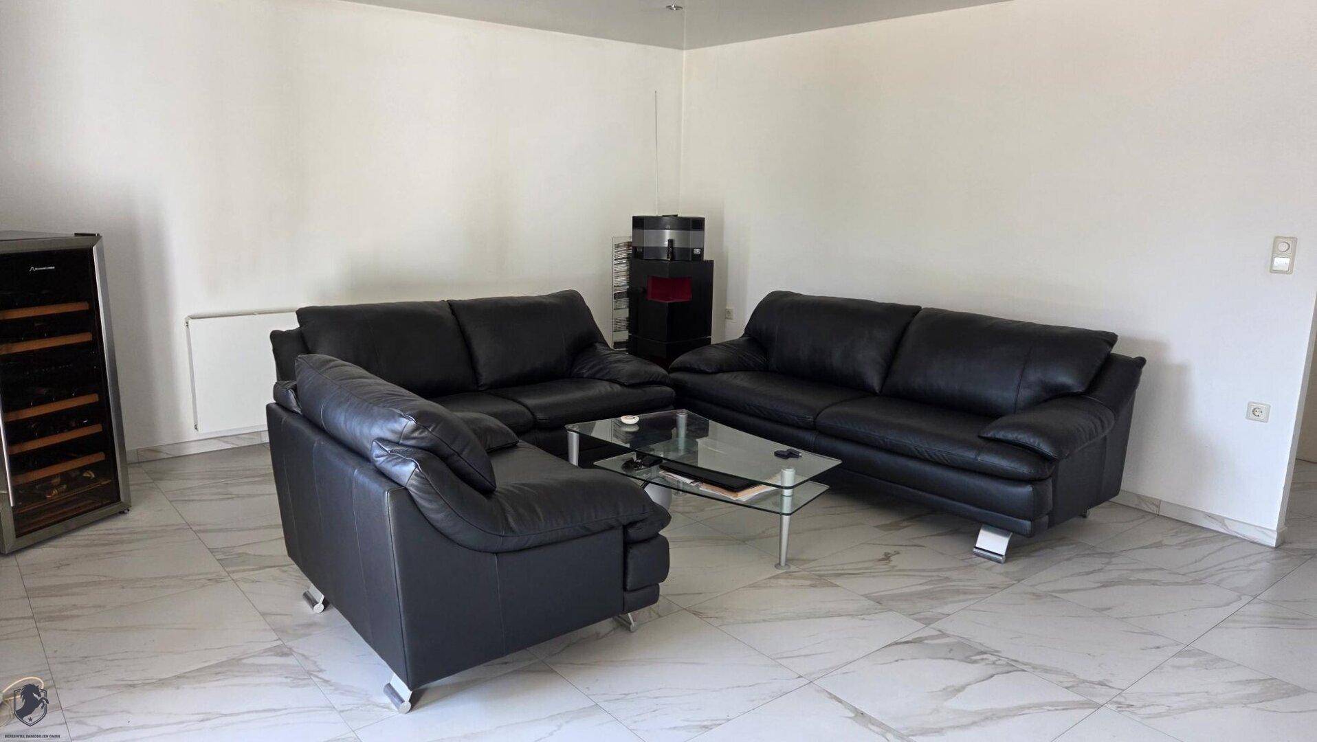Geräumiges Wohnzimmer mit schwarzen Ledersofas und einem Weinkühlschrank.