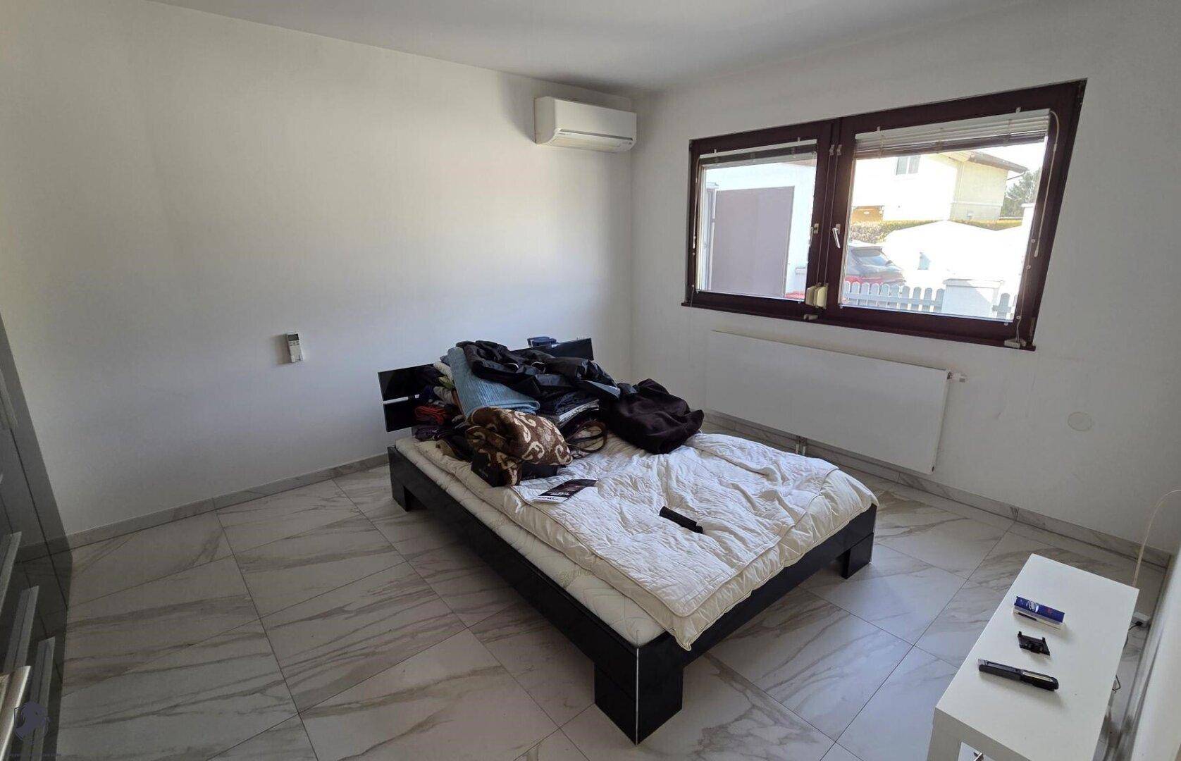 Schlafzimmer mit Bett, Fliesenboden und Klimaanlage an der Wand.