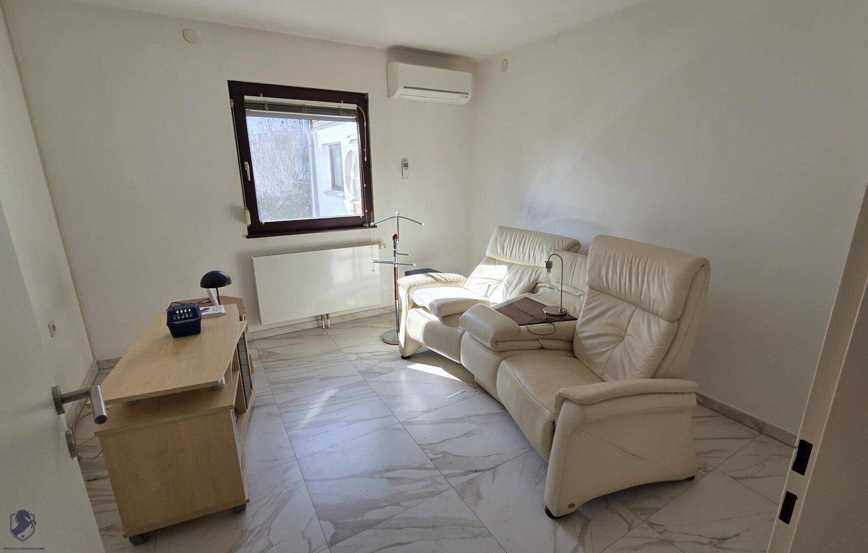 Helles Zimmer mit beigen Ledersesseln, Schreibtisch und Klimaanlage.