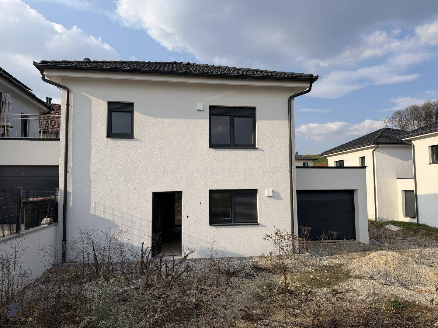Seitenansicht eines modernen Neubauhauses mit weißer Fassade und dunklen Fenstern.