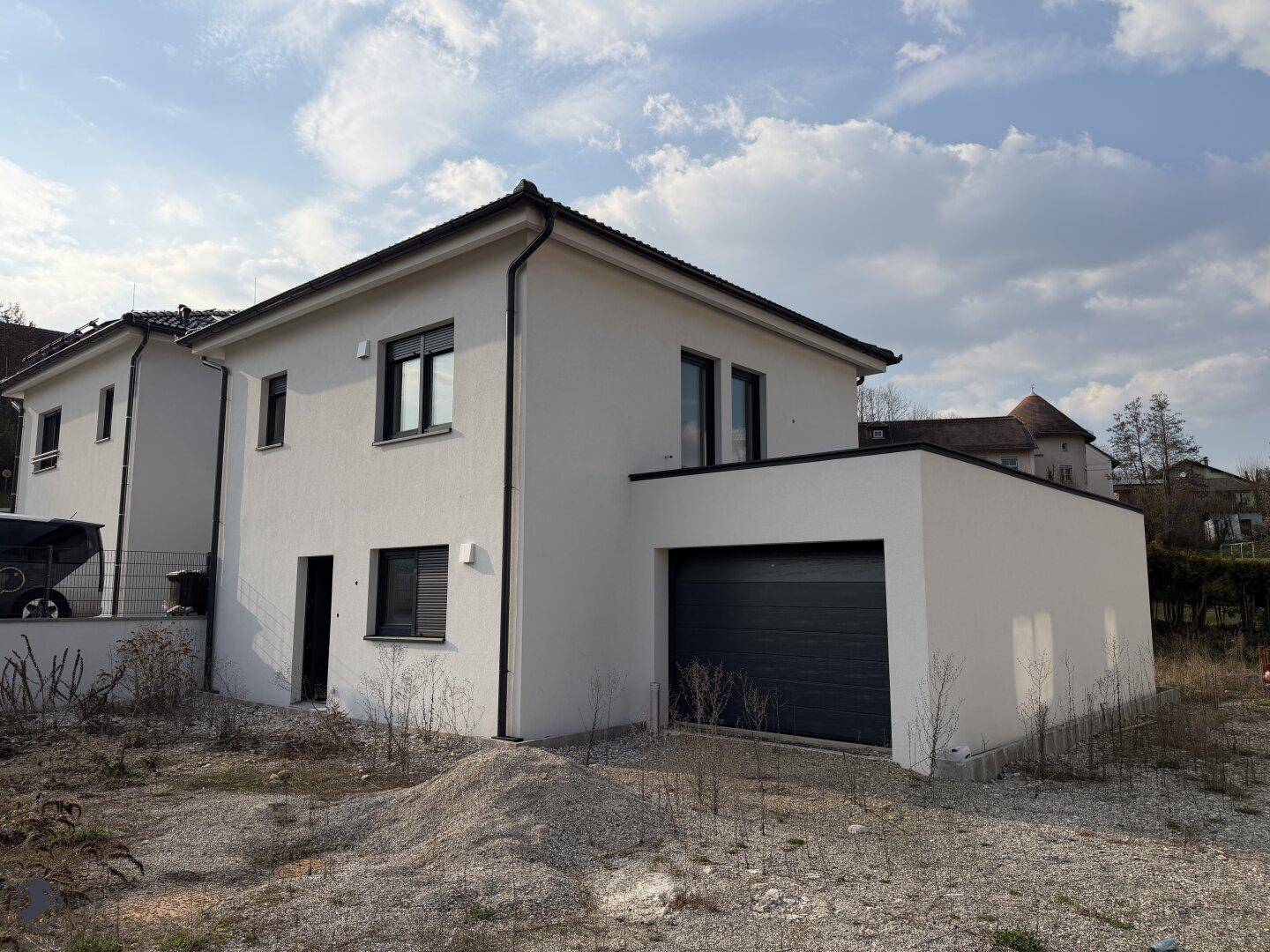 Modernes Einfamilienhaus mit weißer Fassade, integrierter Garage und dunklen Fensterrahmen.