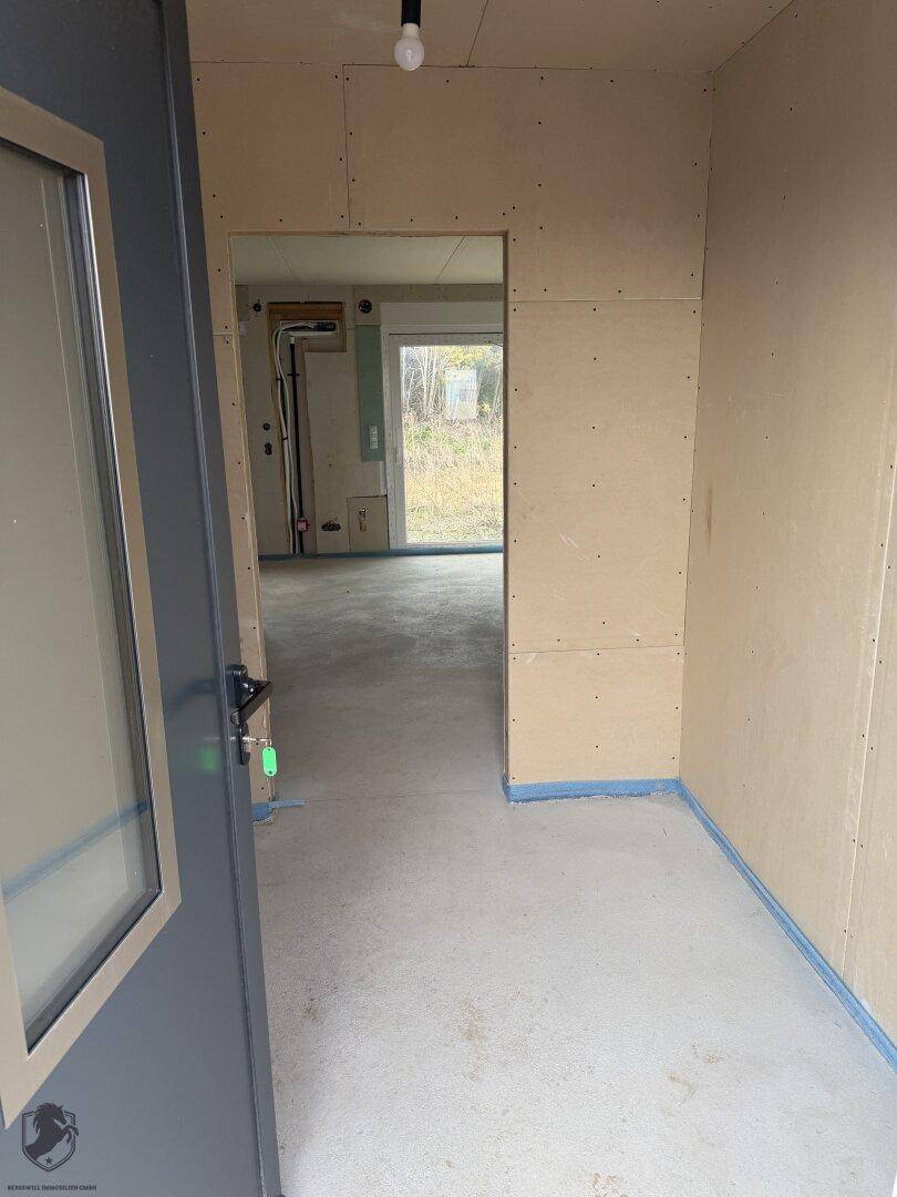 Eingangsbereich eines Hauses im Rohbauzustand mit Blick auf den Garten durch ein Fenster.