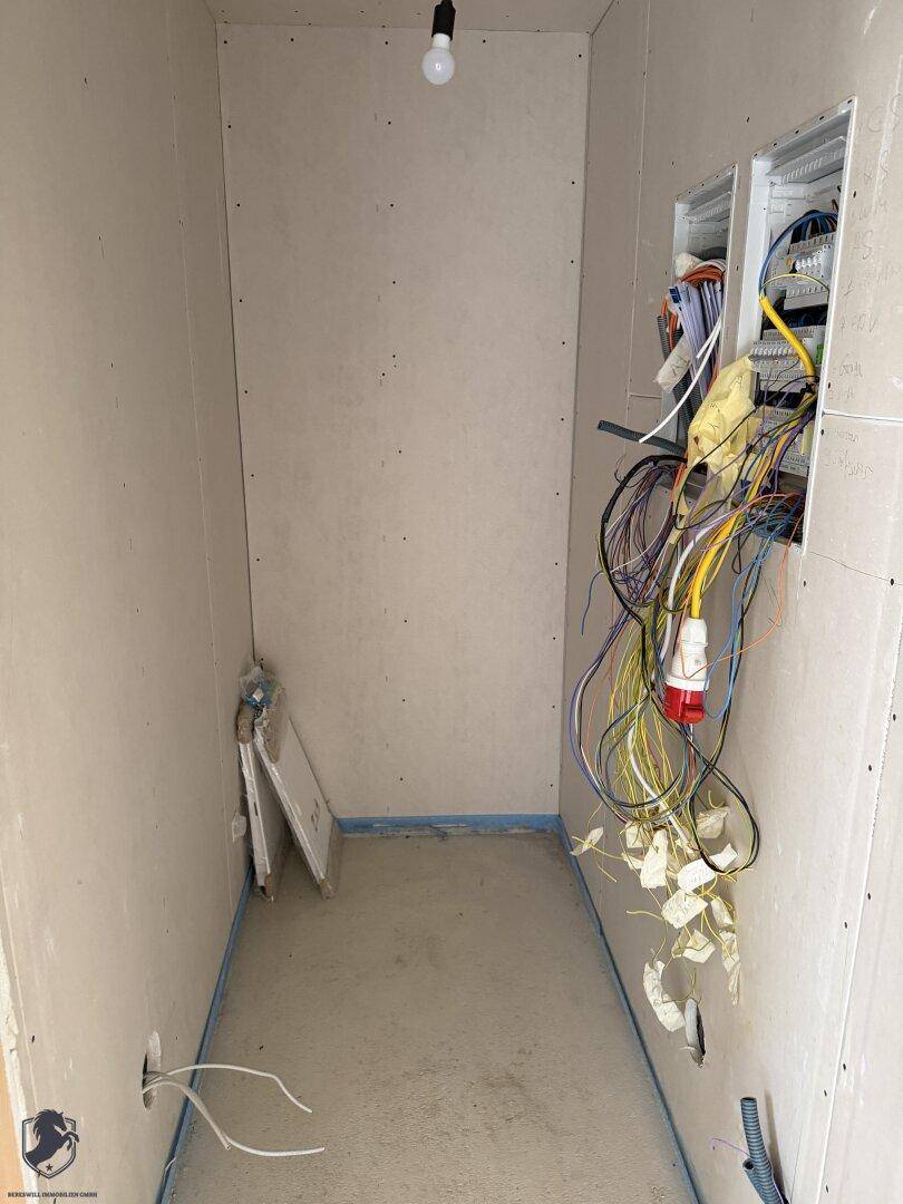 Technikraum im Rohbau mit sichtbaren Elektroleitungen und unfertigen Wänden.