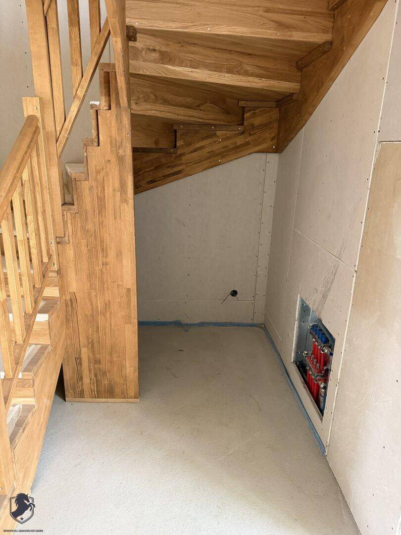 Holztreppe im Rohbau mit sichtbaren Heizungsrohren im Wandbereich.