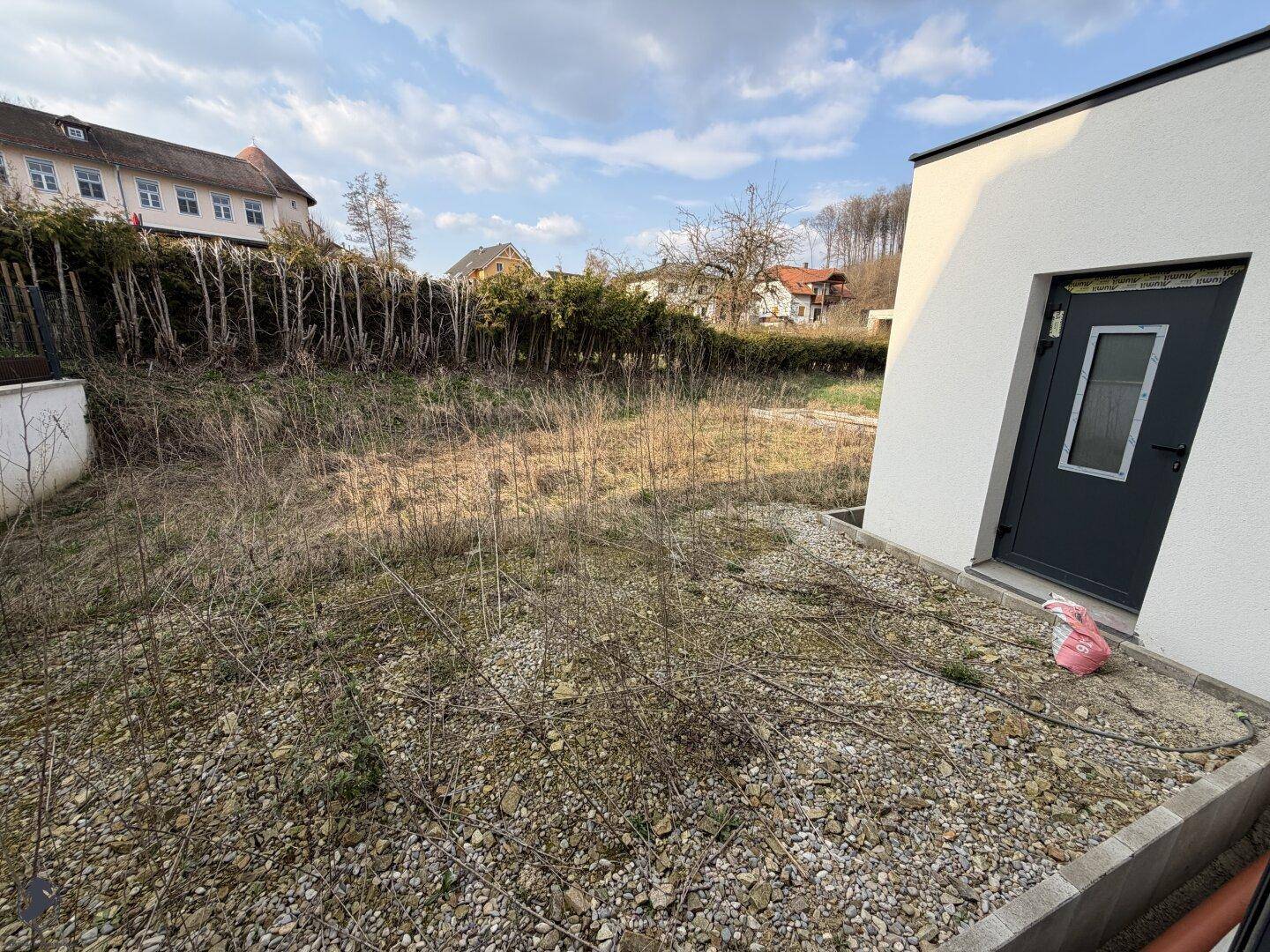 Ungepflegter Gartenbereich neben dem Haus, bereit für die Landschaftsgestaltung.