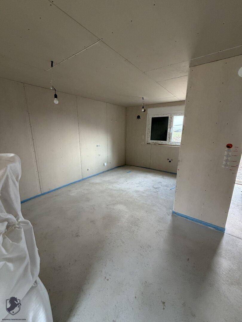 Zimmer im Rohbau mit einem Fenster und Betonboden, bereit für den Innenausbau.
