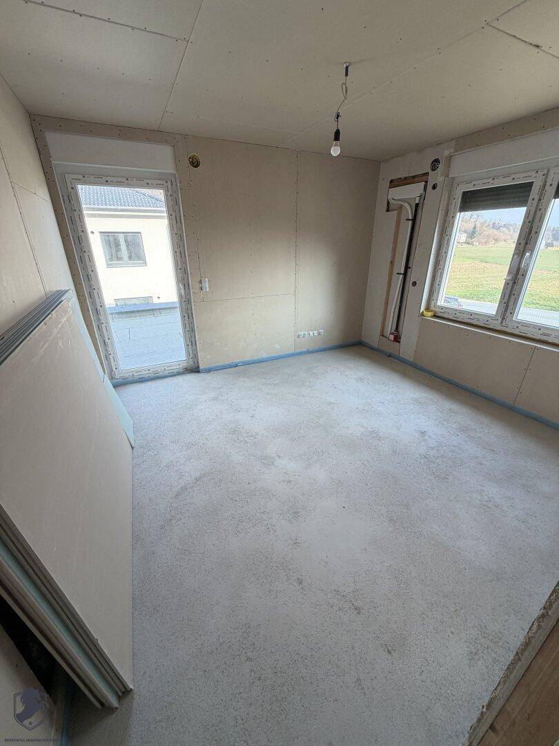 Zimmer im Rohbau mit Zugang nach draußen und großen Fenstern.