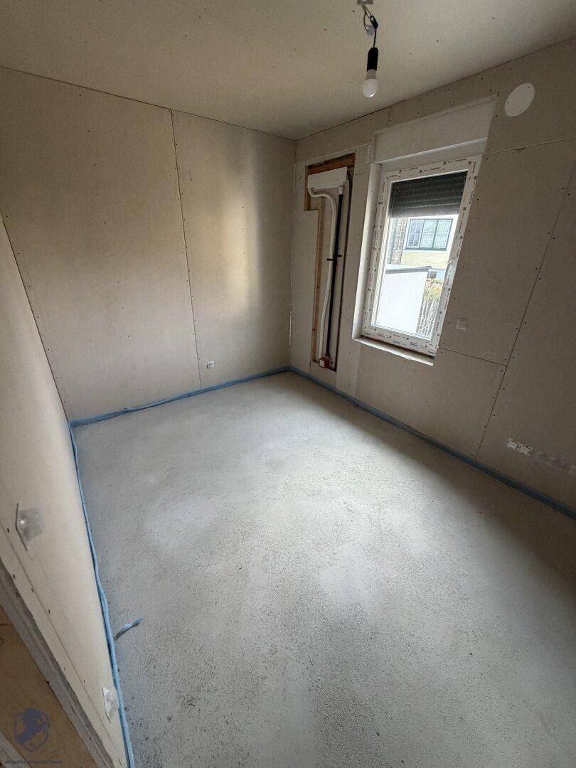 Zimmer im Rohbau mit einem Fenster und unfertigen Wänden.