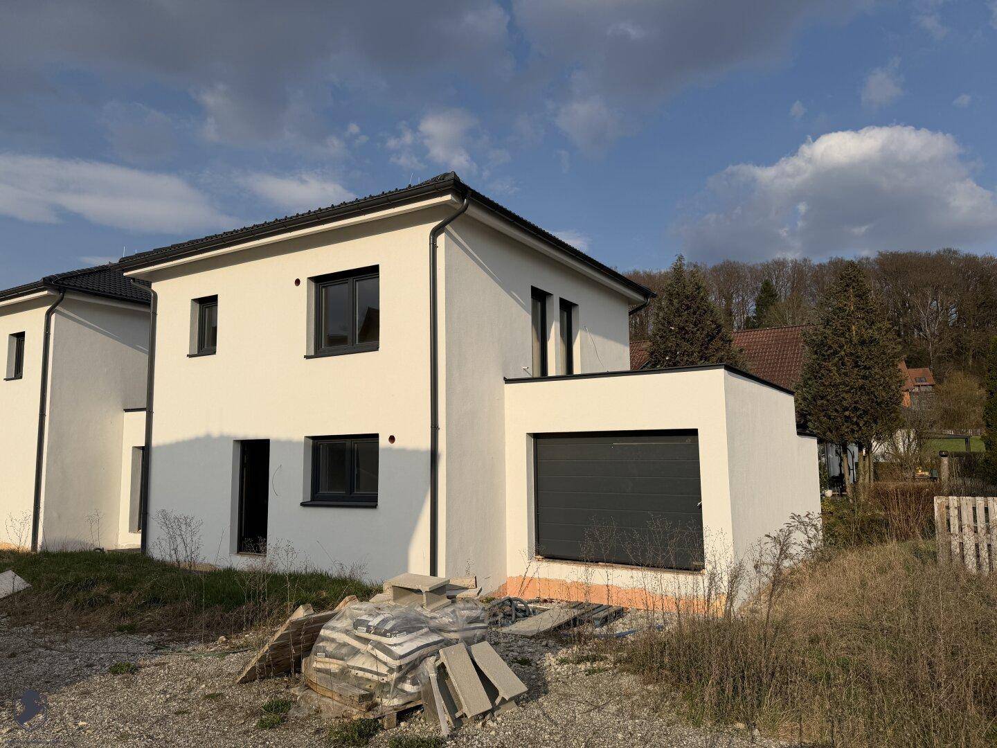 Modernes Einfamilienhaus mit weißer Fassade, dunklen Fenstern und integrierter Garage.