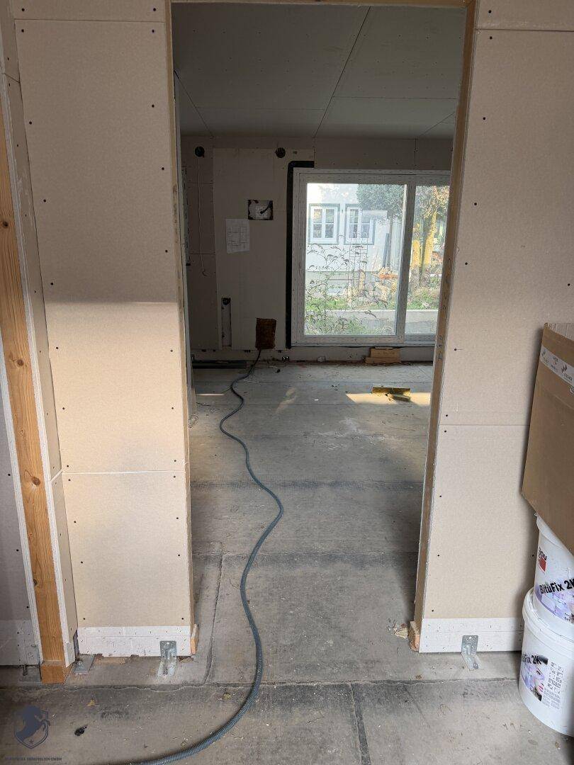 Türöffnung zu einem Zimmer im Rohbau mit Blick auf den Garten durch ein Fenster.