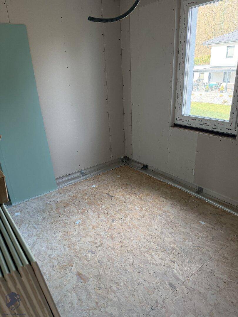 Zimmer im Rohbau mit Fenster und OSB-Plattenboden.