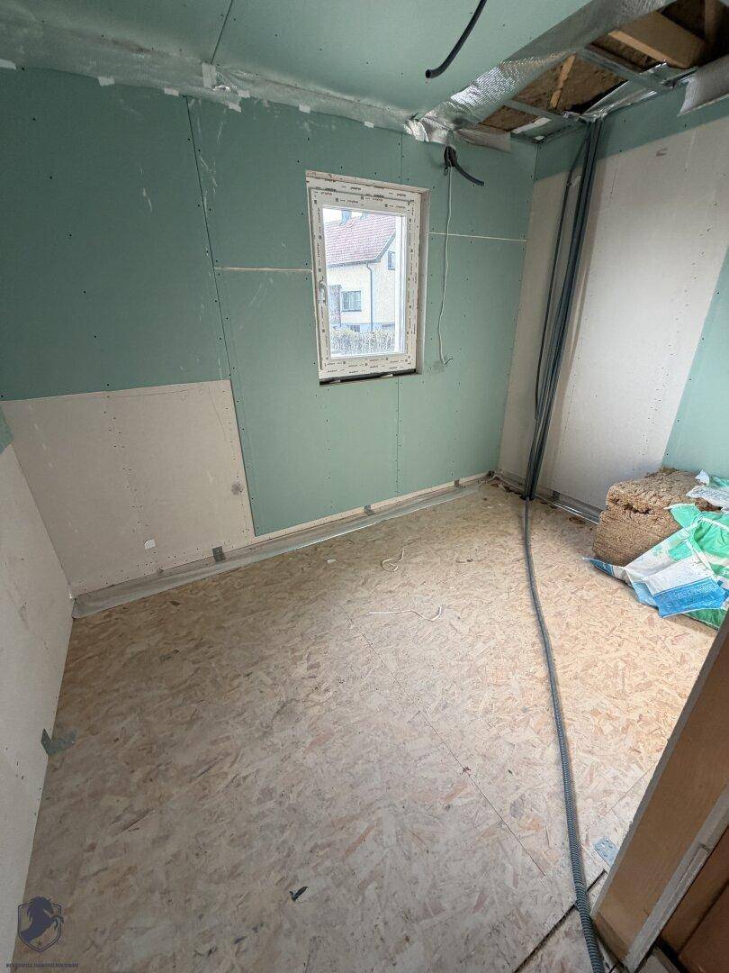 Zimmer im Rohbau mit grünen Gipskartonplatten, Fenster und OSB-Plattenboden.