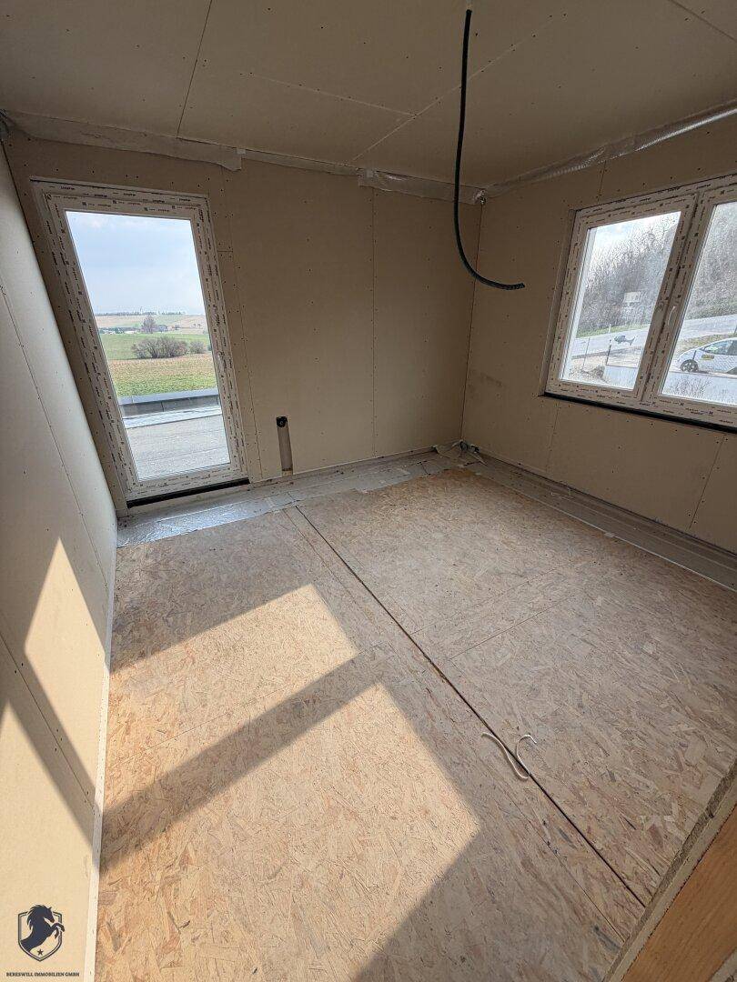 Zimmer im Rohbau mit Fenstern und Zugang zu einem möglichen Dachterrassenbereich.