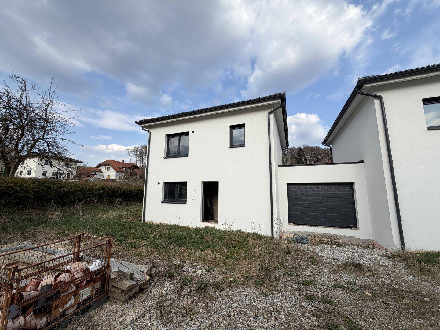 Modernes Einfamilienhaus mit weißer Fassade, dunklen Fenstern und integrierter Garage.