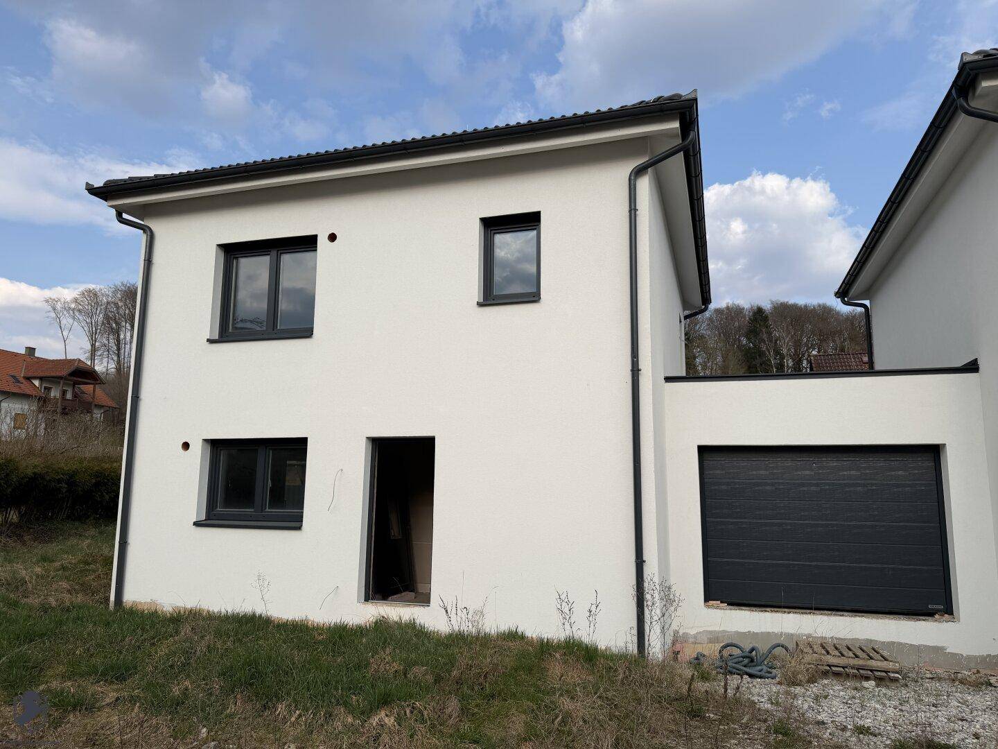 Modernes Einfamilienhaus mit weißer Fassade, dunklen Fenstern und integrierter Garage.