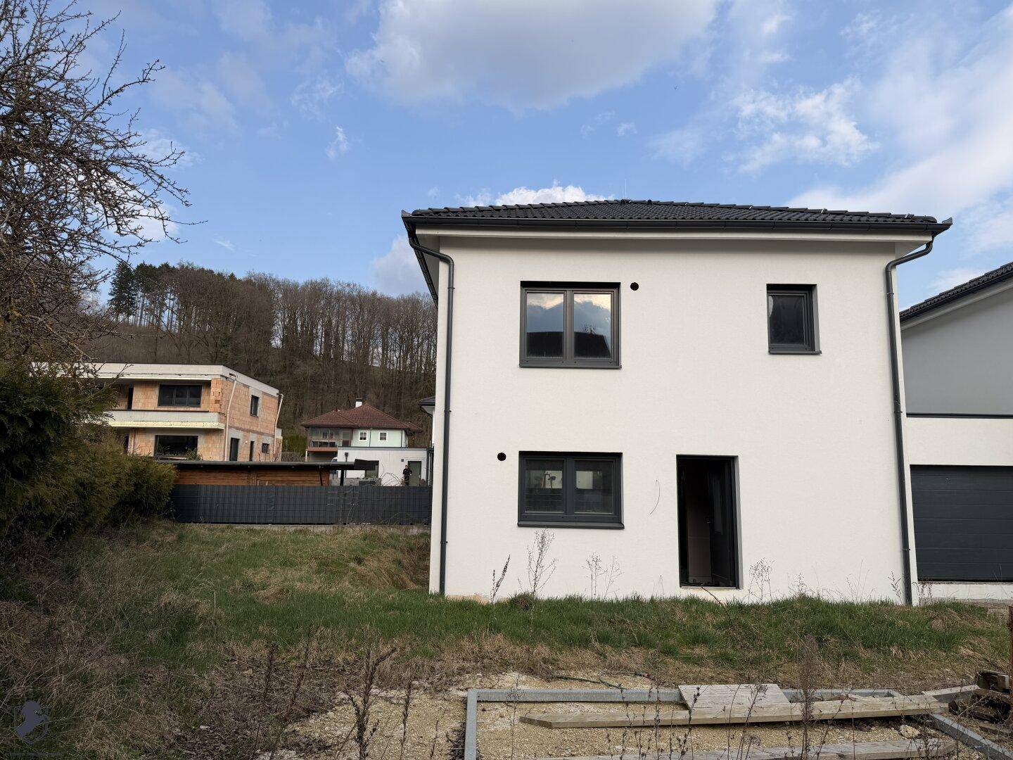 Modernes Einfamilienhaus mit weißer Fassade und Blick auf weitere Gebäude im Hintergrund.