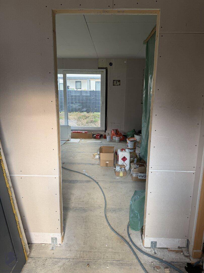 Türöffnung zu einem Zimmer im Rohbau mit Blick auf den Garten durch ein Fenster.